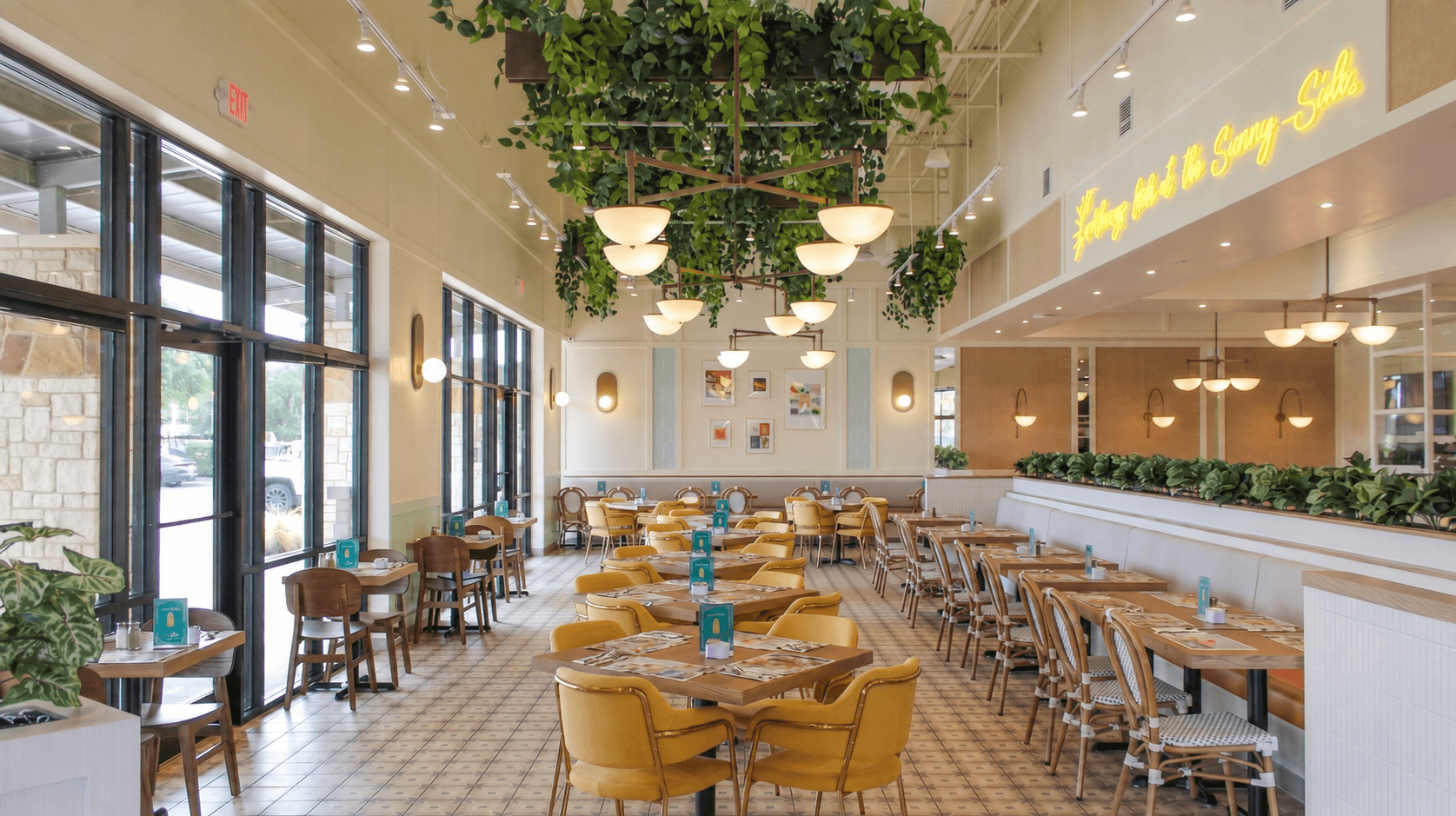 Interior of a Pür & Simple location with yellow chairs down the center of the dining room. Greenery draping above the light fixtures and rows of two person tables to either side of the center row of tables.